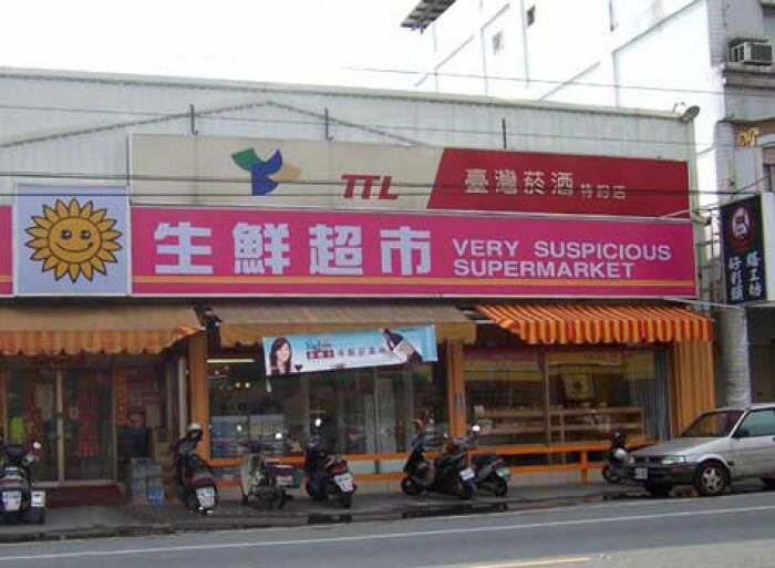 A sign that reads, 'Very Suspicious Market' The text is placed after an Asian language I can't identify, and the sign is placed in front of a storefront with some scooters parked in front.