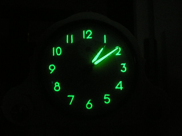 A glowing green watch dial floating in blackness.
